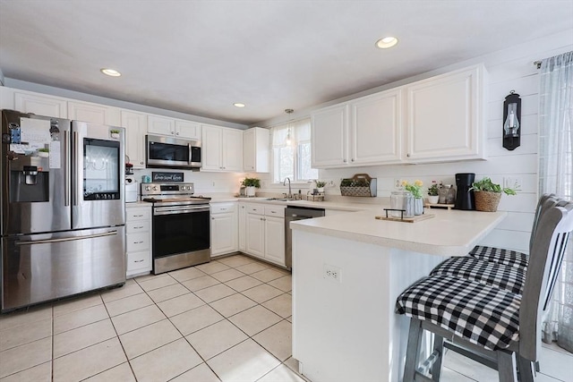 kitchen featuring white cabinets, appliances with stainless steel finishes, sink, kitchen peninsula, and light tile patterned floors