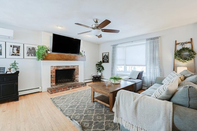 living room featuring wood-type flooring, baseboard heating, ceiling fan, and a brick fireplace