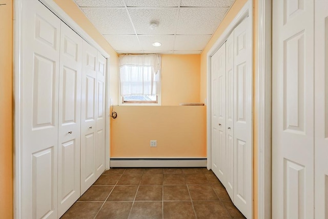 hallway with a baseboard radiator, a paneled ceiling, and dark tile patterned floors