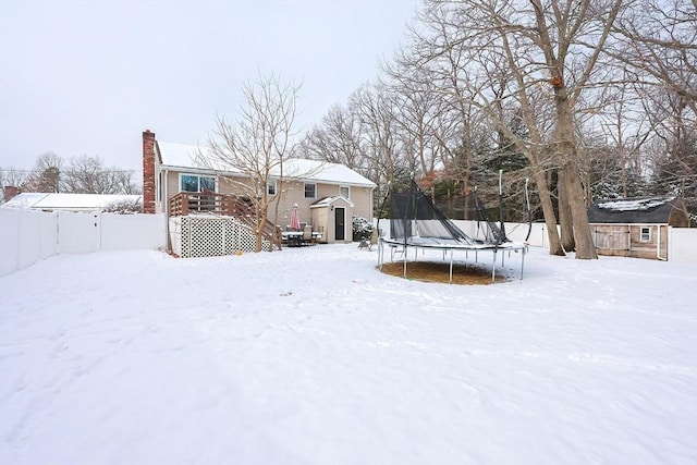 yard layered in snow with a shed, a deck, and a trampoline