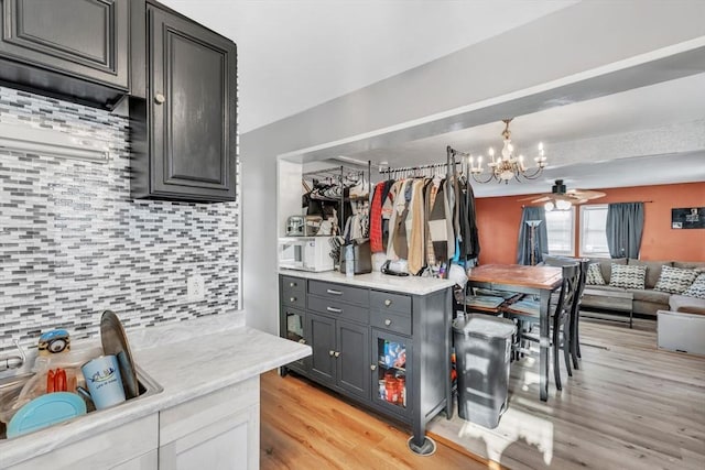 kitchen with ceiling fan with notable chandelier, gray cabinetry, tasteful backsplash, decorative light fixtures, and light wood-type flooring