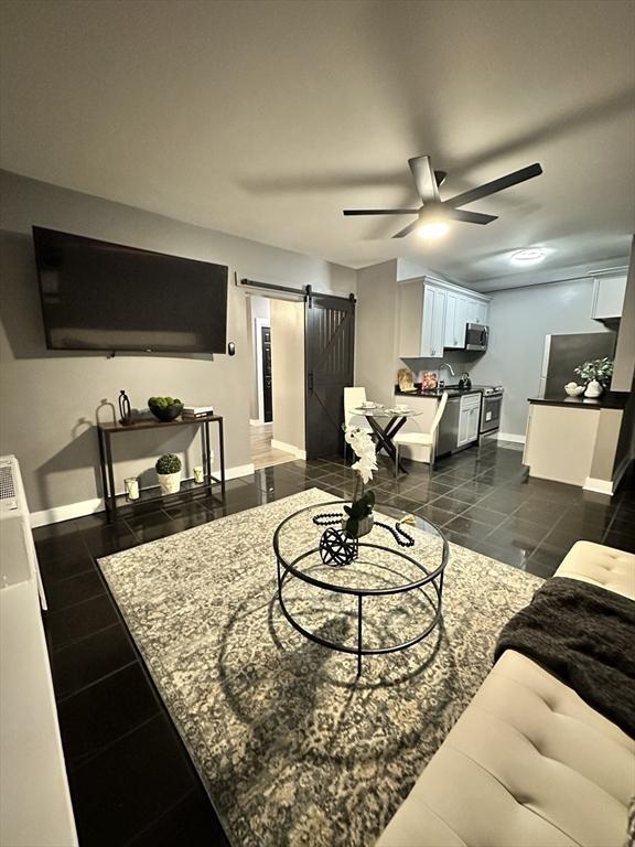 living room featuring a ceiling fan, dark tile patterned floors, baseboards, and a barn door