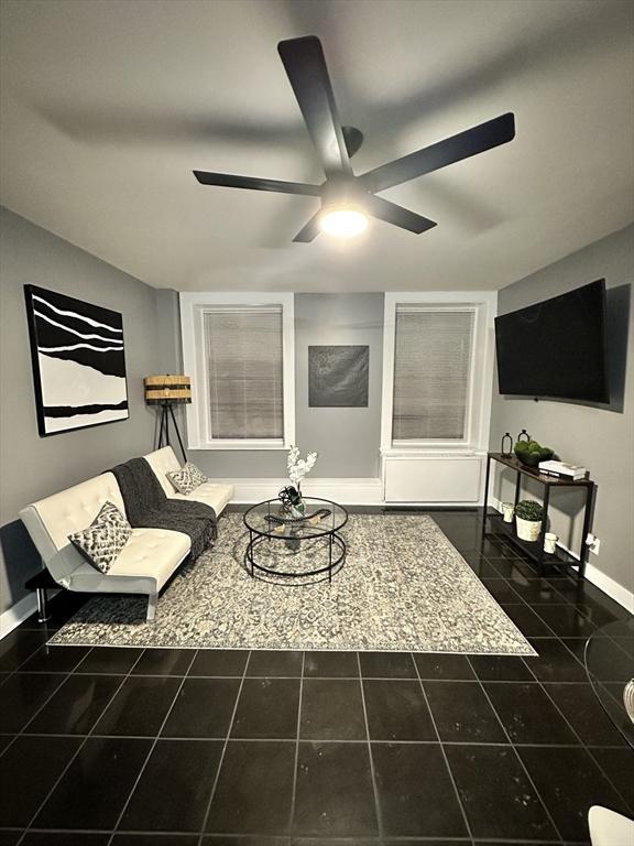 living area featuring a ceiling fan, dark tile patterned floors, and baseboards