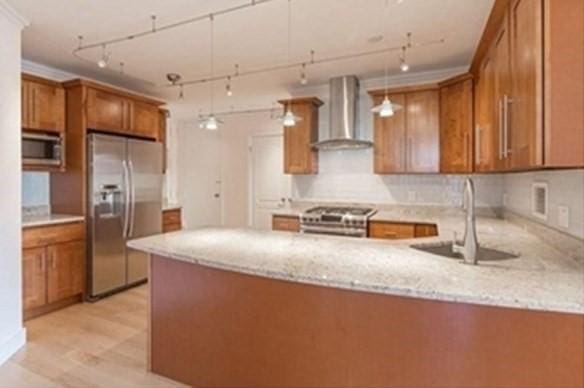 kitchen featuring light stone counters, appliances with stainless steel finishes, a sink, a peninsula, and wall chimney exhaust hood