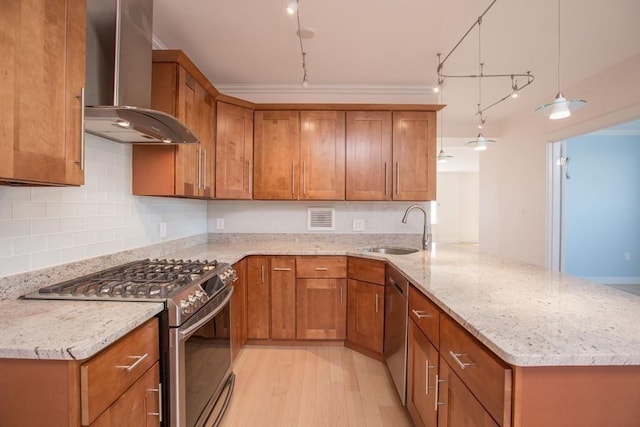 kitchen with brown cabinetry, wall chimney exhaust hood, appliances with stainless steel finishes, hanging light fixtures, and a sink