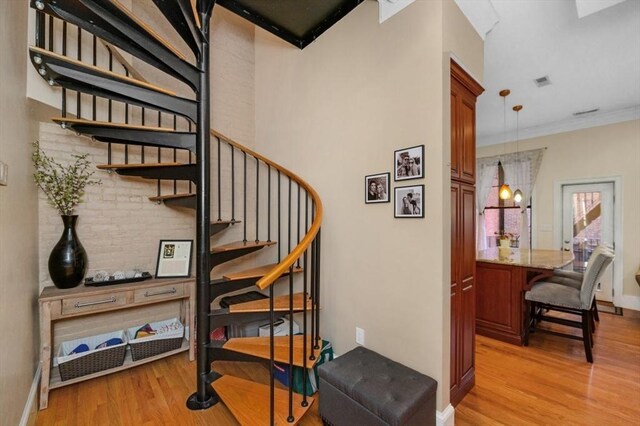 stairway with baseboards, wood finished floors, visible vents, and ornamental molding