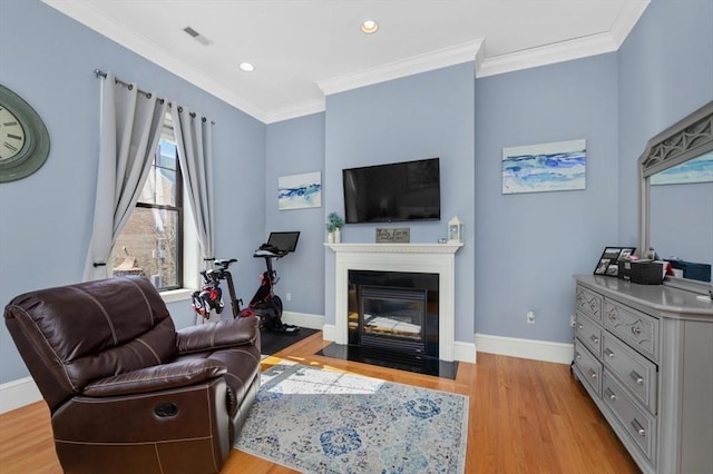 living area with a fireplace with flush hearth, baseboards, light wood-type flooring, and ornamental molding