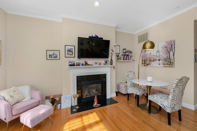 living area featuring visible vents, a fireplace with flush hearth, wood finished floors, and crown molding