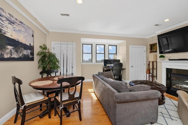 living area featuring visible vents, ornamental molding, a glass covered fireplace, light wood finished floors, and baseboards