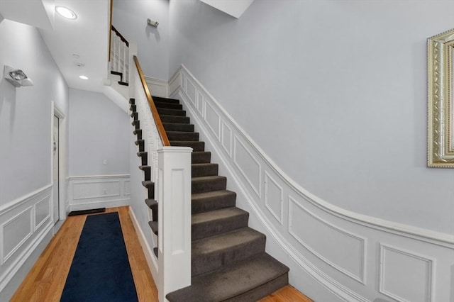 staircase featuring a decorative wall, recessed lighting, wood finished floors, and a wainscoted wall