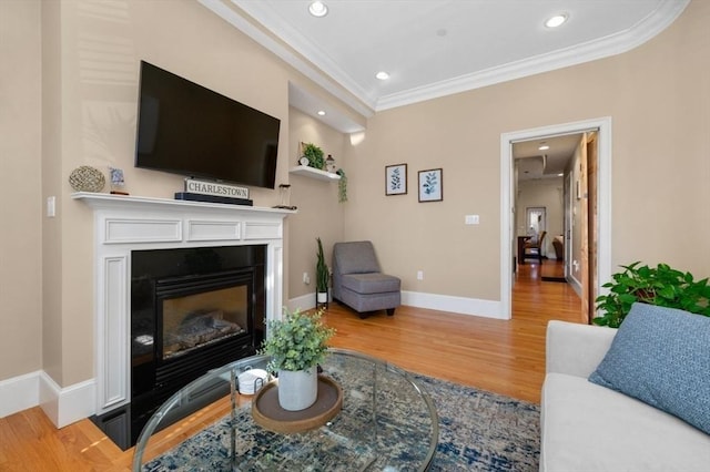 living area featuring wood finished floors, baseboards, recessed lighting, a glass covered fireplace, and crown molding