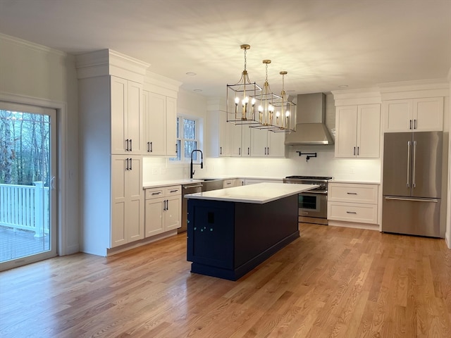 kitchen featuring stainless steel appliances, white cabinetry, wall chimney exhaust hood, hanging light fixtures, and a kitchen island