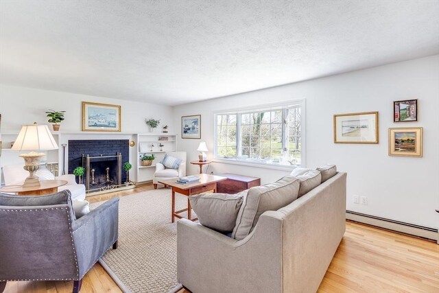 living room with a textured ceiling, light wood-style flooring, a baseboard heating unit, and a fireplace