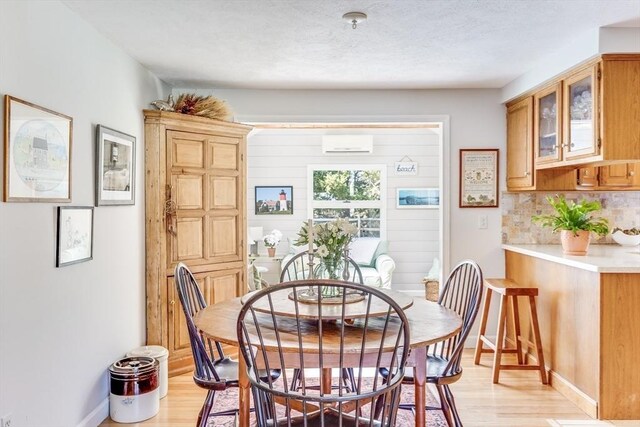 dining space with baseboards, a wall unit AC, and light wood-type flooring