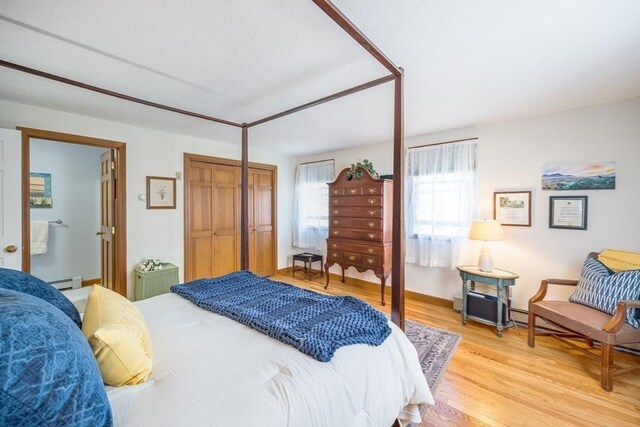 bedroom featuring a closet, light wood-style flooring, and a baseboard heating unit