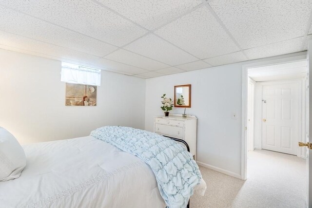 bedroom with baseboards, a drop ceiling, and light carpet
