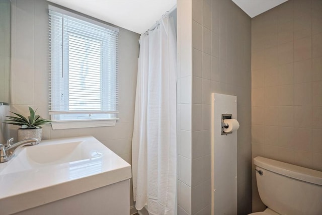 bathroom with vanity, toilet, a shower with shower curtain, and tile walls