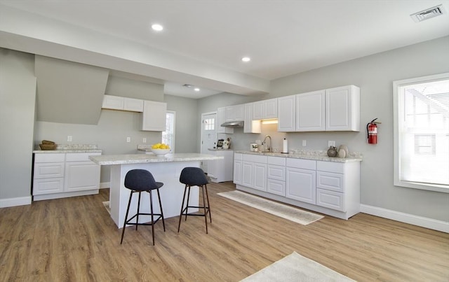 kitchen with a kitchen island, a breakfast bar, sink, white cabinets, and light hardwood / wood-style flooring