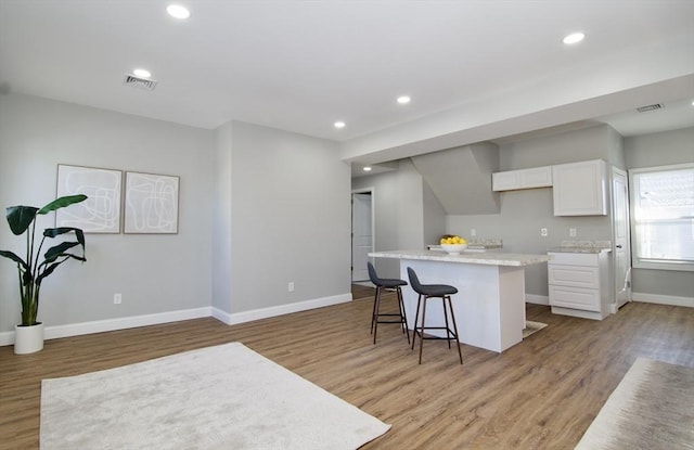 kitchen with white cabinetry, a breakfast bar area, light hardwood / wood-style flooring, and a kitchen island