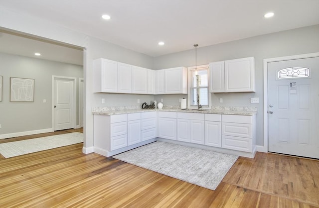 kitchen with white cabinetry, sink, hanging light fixtures, and light wood-type flooring