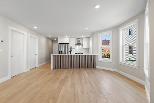 kitchen with stainless steel refrigerator with ice dispenser, tasteful backsplash, wall chimney range hood, light hardwood / wood-style floors, and white cabinetry