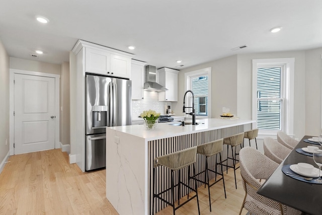 kitchen featuring stainless steel fridge, light wood-type flooring, wall chimney range hood, and white cabinetry