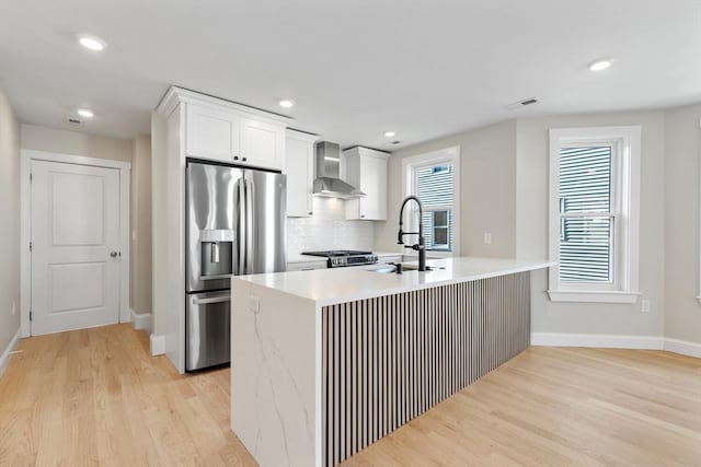 kitchen featuring appliances with stainless steel finishes, light wood-type flooring, wall chimney exhaust hood, sink, and white cabinets