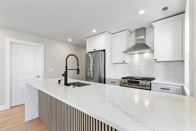 kitchen featuring light stone counters, stainless steel appliances, wall chimney range hood, light hardwood / wood-style flooring, and white cabinetry