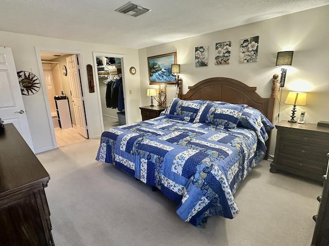 bedroom with light colored carpet, visible vents, a textured ceiling, and a spacious closet