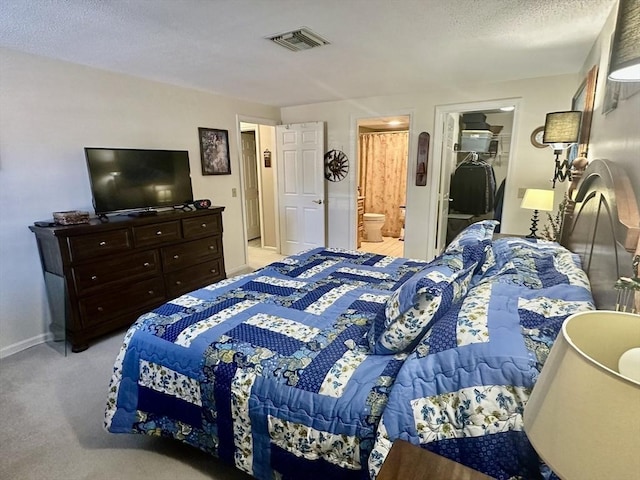 bedroom featuring a walk in closet, light colored carpet, visible vents, ensuite bath, and baseboards