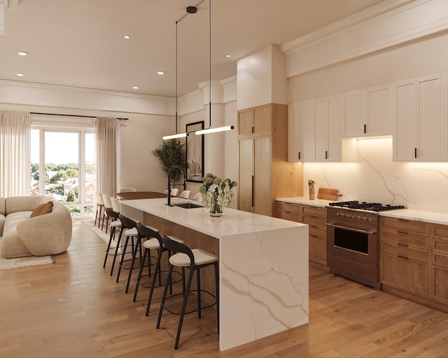 kitchen with white cabinetry, high end stainless steel range oven, light hardwood / wood-style flooring, and a center island with sink