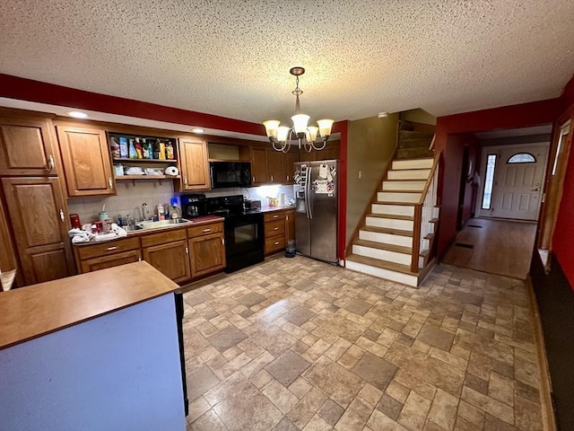 kitchen featuring a sink, a textured ceiling, a chandelier, black appliances, and stone tile flooring