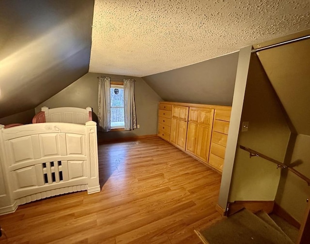 bonus room with baseboards, light wood-type flooring, a textured ceiling, and lofted ceiling