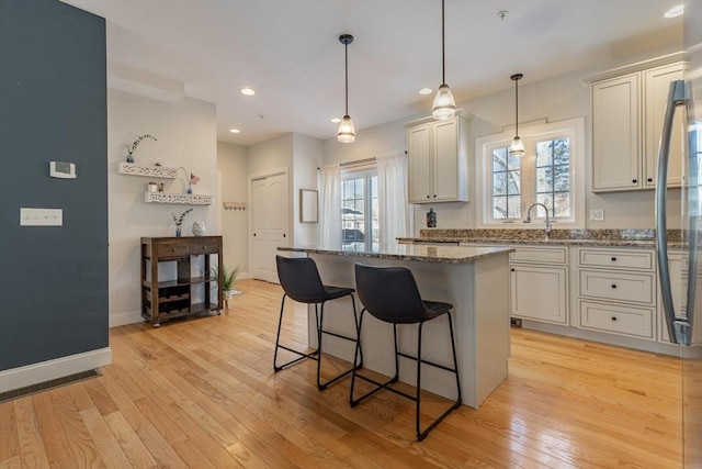 kitchen featuring stone counters, hanging light fixtures, white cabinets, a kitchen island, and light wood-type flooring