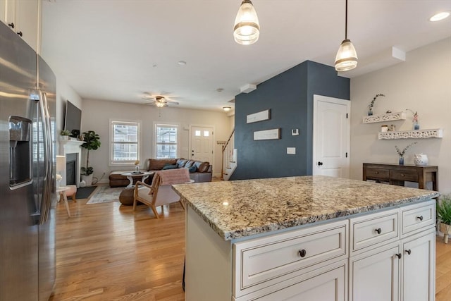 kitchen with decorative light fixtures, a kitchen island, white cabinets, and stainless steel refrigerator with ice dispenser