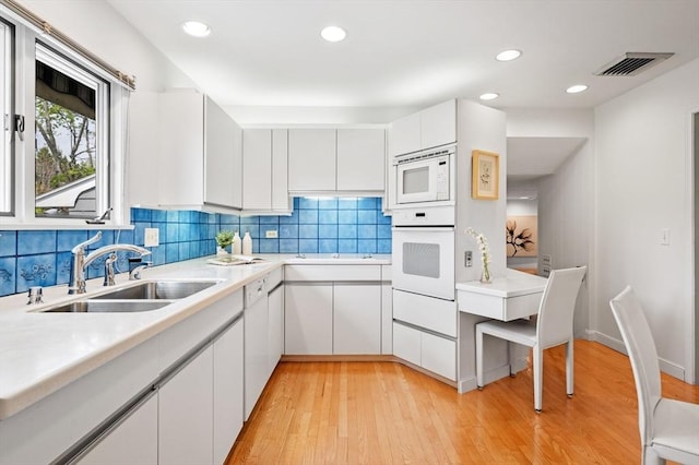 kitchen with a sink, white cabinetry, visible vents, white appliances, and light countertops