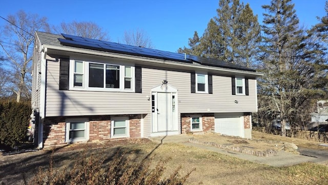 bi-level home with a garage, solar panels, and brick siding