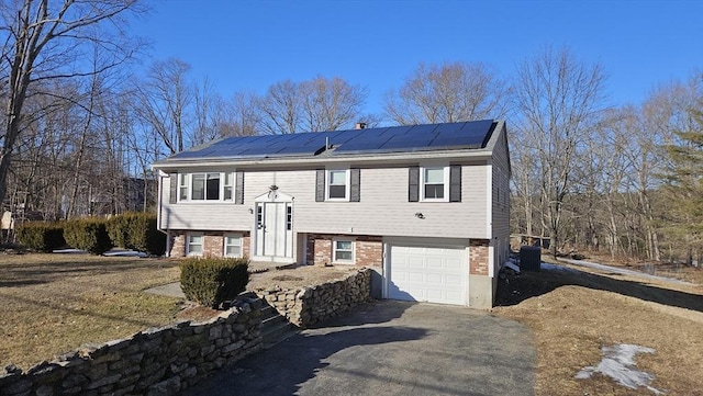 split foyer home with roof mounted solar panels, brick siding, and an attached garage