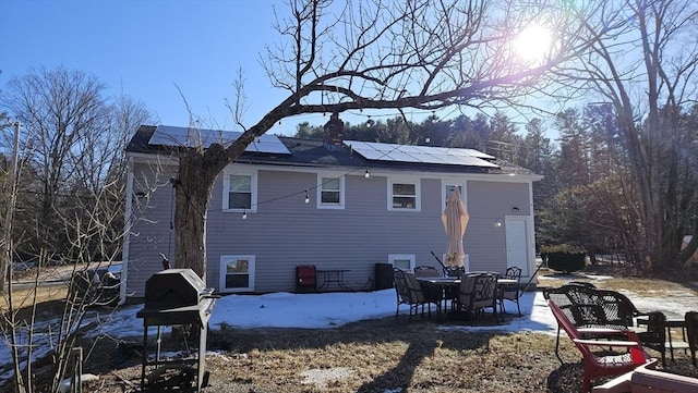 back of property with a patio, a chimney, and roof mounted solar panels