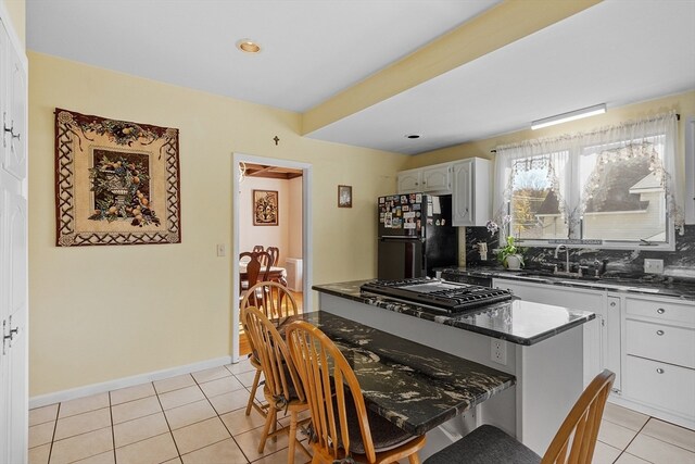 kitchen with stainless steel gas cooktop, sink, black fridge, light tile patterned floors, and decorative backsplash