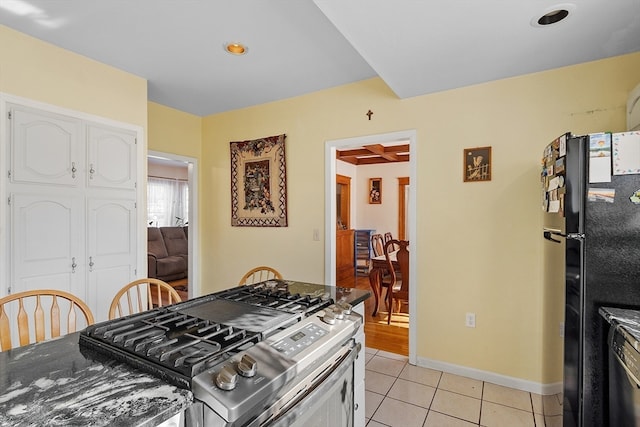 kitchen with white cabinets, light tile patterned flooring, and black fridge