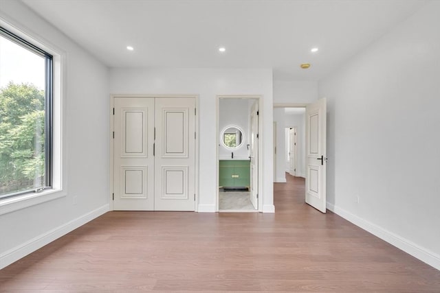 unfurnished bedroom with multiple windows, a closet, and hardwood / wood-style floors