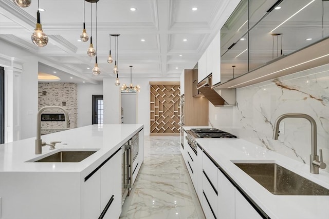 kitchen featuring a kitchen island with sink, sink, white cabinets, and hanging light fixtures