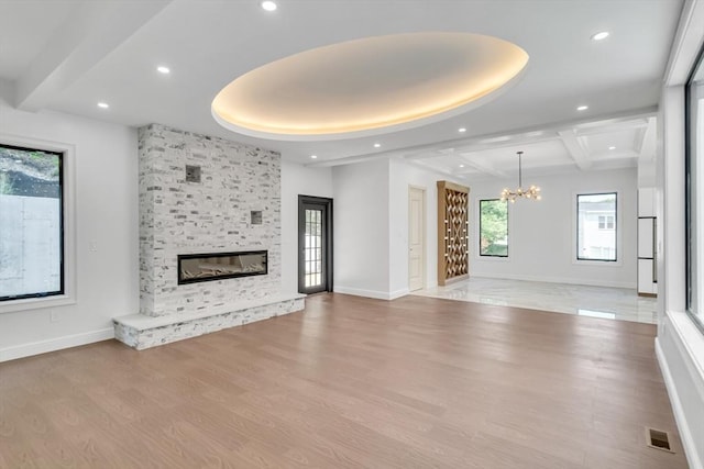 unfurnished living room with beamed ceiling, a chandelier, a stone fireplace, and light hardwood / wood-style flooring