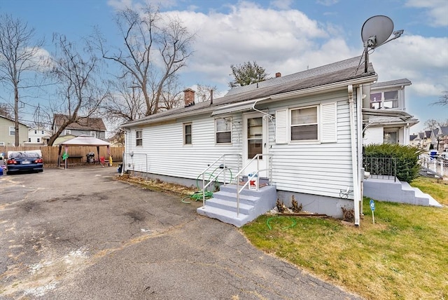 view of front of property featuring entry steps, driveway, a chimney, and fence