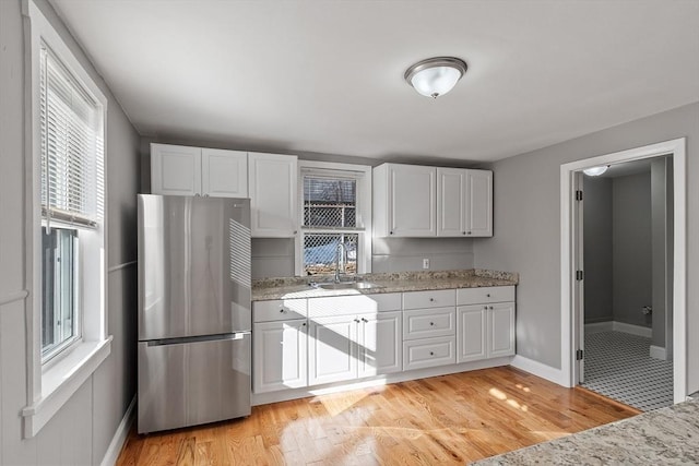 kitchen featuring white cabinets, light wood-type flooring, freestanding refrigerator, and a sink