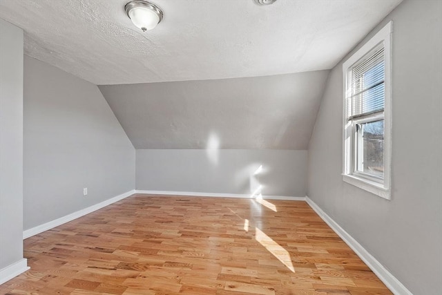 bonus room featuring a textured ceiling, baseboards, light wood-style floors, and vaulted ceiling