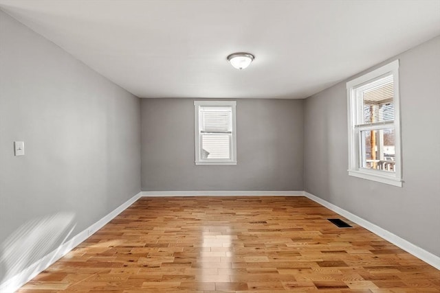 unfurnished room featuring visible vents, plenty of natural light, light wood-style floors, and baseboards