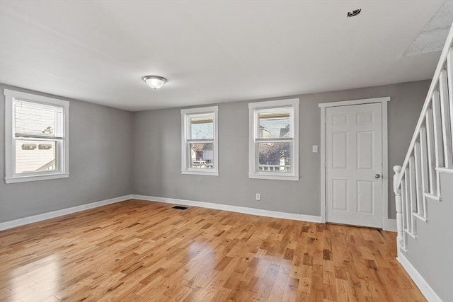 empty room with stairs, light wood-style flooring, and baseboards