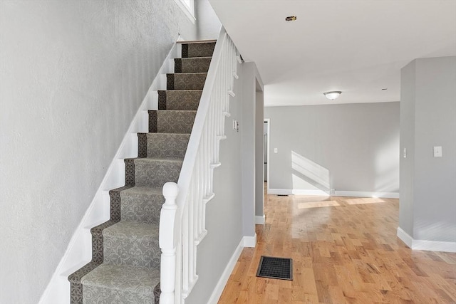 staircase with wood finished floors, visible vents, and baseboards